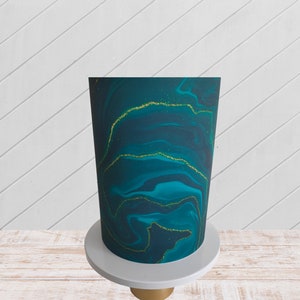 Può includere: Una torta marmorizzata verde acqua e oro su un supporto per torte bianco. La torta è decorata con glitter dorati.
