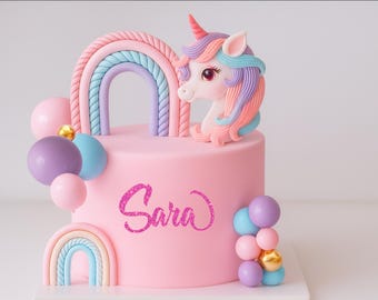 May include: A pink cake decorated with a unicorn head, rainbow, and colourful spheres. The cake has the name "Sara" written in glittery pink script. The unicorn has a pink horn and colourful mane.