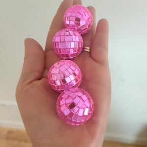 Pu&ograve; includere: Quattro ornamenti a forma di palla da discoteca rosa con piastrelle a specchio.