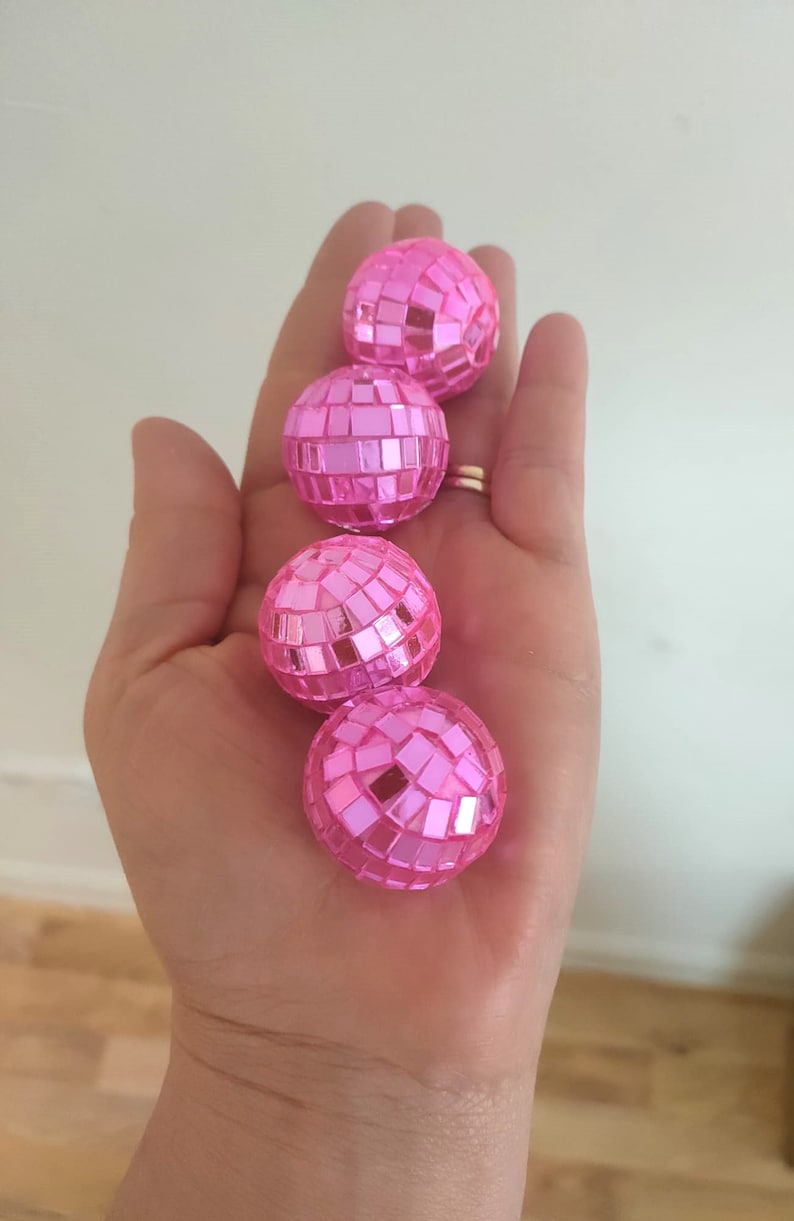 Pu&ograve; includere: Quattro ornamenti a forma di palla da discoteca rosa con piastrelle a specchio.