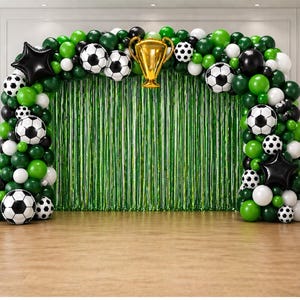 Può includere: Un arco di palloncini a tema calcio con palloncini verdi, bianchi e neri e dettagli a pallone da calcio. Un trofeo d'oro è al centro, con uno sfondo di frange verdi. Palloncini neri a forma di stella.