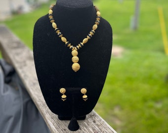 May include: A gold necklace with black and gold beads and a matching pair of earrings. The necklace has a pendant with a layered design.