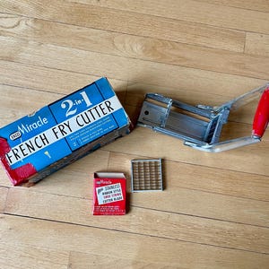 May include: A vintage French fry cutter set, including a blue and red box with "Miracle FRENCH FRY CUTTER" text, a stainless steel cutter, and a red-handled cutting tool. The set also includes a small red box with "STAINLESS RIBBON STYLE SHOE STRING CUTTER BLADE" text.