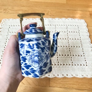 May include: A small blue and white porcelain teapot with a gold handle. The teapot has a floral design and is perfect for a tea party.