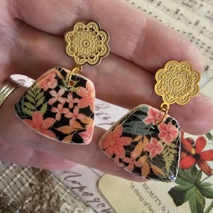 May include: A pair of earrings with black and pink floral patterned ceramic teardrop shapes and gold filigree accents.