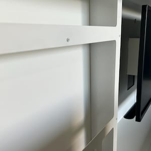 May include: A white, built-in cabinet with a black computer monitor. The cabinet has shelves and a rectangular opening. The monitor is mounted inside the cabinet. The image is a close-up shot.