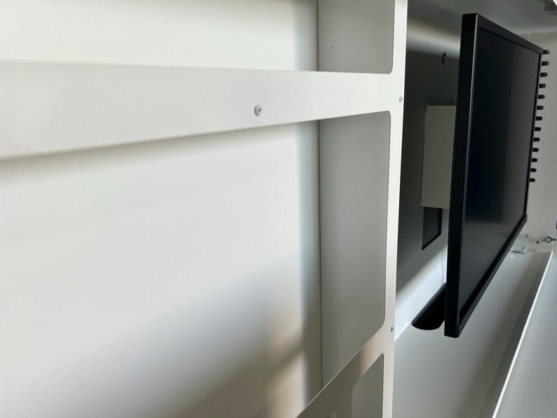 May include: A white, built-in cabinet with a black computer monitor. The cabinet has shelves and a rectangular opening. The monitor is mounted inside the cabinet. The image is a close-up shot.