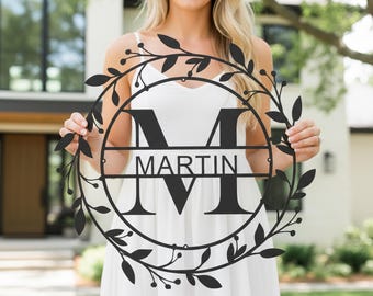 May include: A black metal family name sign with the name "MARTIN" and the initial "M" in a circular design. The sign is surrounded by a decorative leaf and berry wreath.