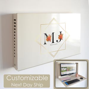 Könnte beinhalten: Ein weißer, an der Wand montierter Schreibtisch mit einem goldenen geometrischen Design und den Initialen "MJ" mit floralen Akzenten. Der Text "Marry & Jason" befindet sich unter den Initialen. Der Schreibtisch ist mit einem Laptop, einer Tastatur und einer Maus ausgestattet.