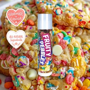 Peut inclure: Un tube de baume à lèvres cylindrique avec une étiquette portant le texte Fruity Pebbles en lettres blanches sur fond violet. Le tube est placé sur un fond de biscuits aux morceaux de céréales colorés et aux pépites de chocolat blanc.