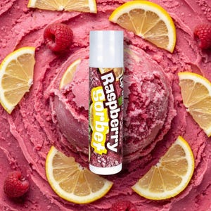 Könnte beinhalten: Ein Lippenbalsam-Tiegel mit der Aufschrift "Raspberry Sorbet" ist von einer Kugel rosa Sorbet, frischen Himbeeren und Zitronenscheiben umgeben. Der Lippenbalsam-Tiegel hat eine weiße Kappe und ein braun-rosa Etikett.