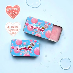 Puede incluir: Dos latas metálicas rectangulares de bálsamo labial Berry Gumball con un fondo azul claro con patrones de burbujas rosas. Las etiquetas muestran el texto Berry Gumball, QueenBalm.ca y Net Wt. 0.2oz. Una lata está abierta, revelando el bálsamo rosa.