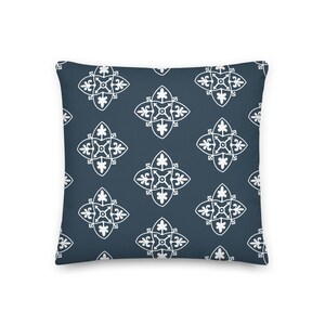 May include: A square decorative pillow with a dark blue background and a repeating white floral pattern. The pattern consists of stylized four-petal flowers with ornate details. The pillow is a home decor item.