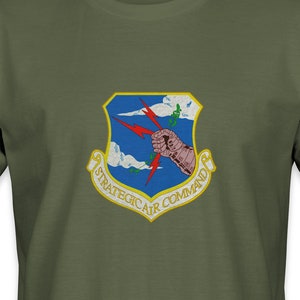May include: A green t-shirt with a gold and blue patch featuring a stylized fist holding lightning bolts and the text "Strategic Air Command".