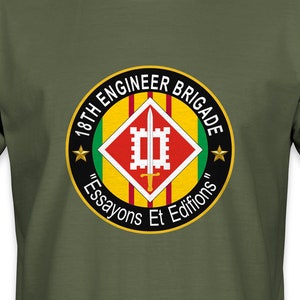 May include: Olive green t-shirt featuring a circular emblem with the text "18th Engineer Brigade" and "Essayons Et Edifions". The emblem has a red and yellow design with a white castle-like structure in the center.