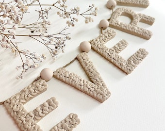 May include: A beige floral letter banner spelling "EVER" with small wooden beads strung between each letter.