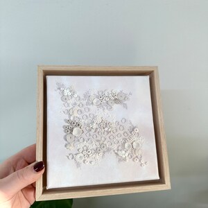 May include: A white framed canvas with a textured white design of circles and other shapes. The design resembles coral or seashells.