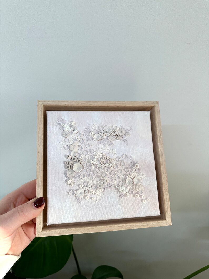 May include: A white framed canvas with a textured white design of circles and other shapes. The design resembles coral or seashells.