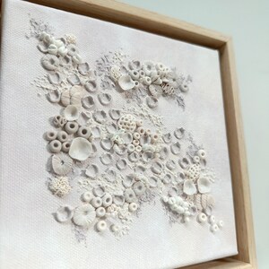 May include: A framed white canvas with a textured, raised design of white and light gray coral shapes. The coral is arranged in a cluster on a white background.