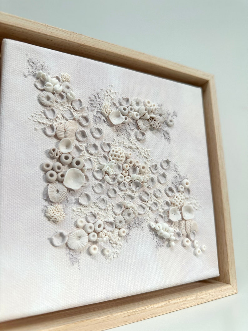 May include: A framed white canvas with a textured, raised design of white and light gray coral shapes. The coral is arranged in a cluster on a white background.