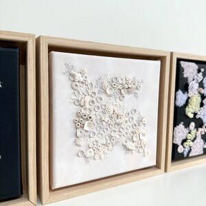 May include: A white framed canvas with a white and gray textured design. The design resembles a cluster of coral or seashells.
