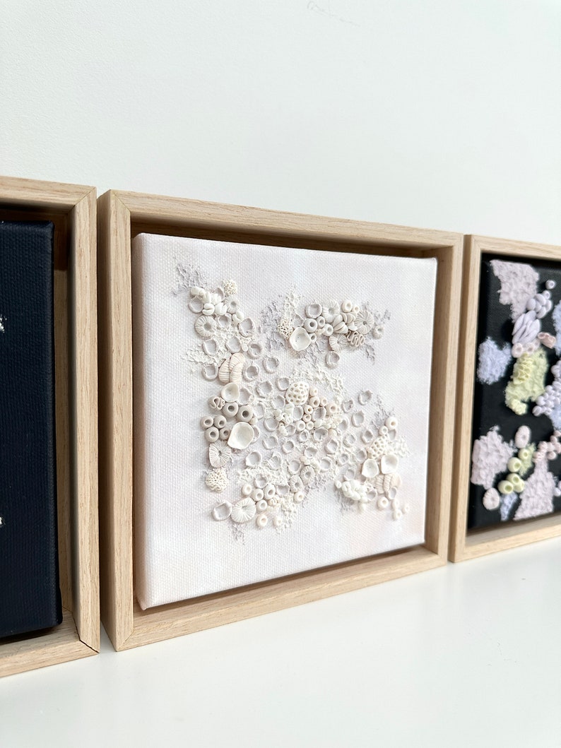 May include: A white framed canvas with a white and gray textured design. The design resembles a cluster of coral or seashells.