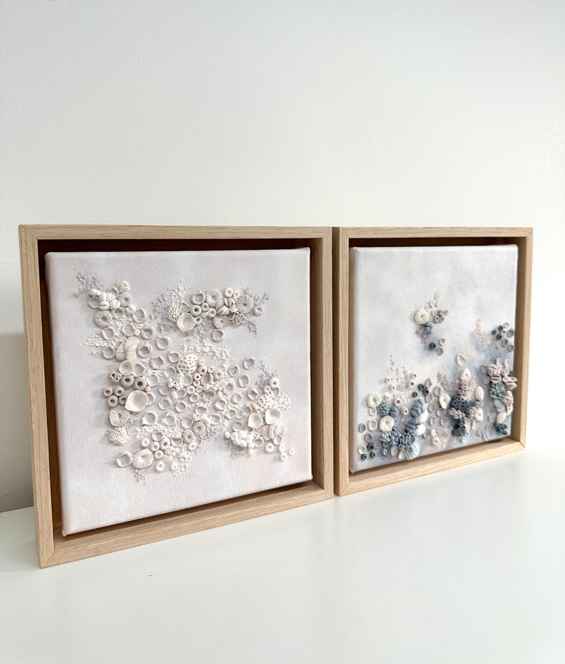 May include: Two framed canvas paintings with a textured, 3D effect. The left painting features white and cream textured shapes, while the right painting features blue and gray textured shapes.