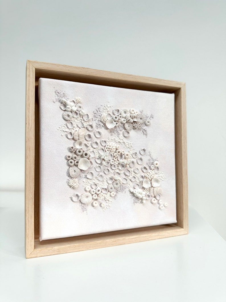 May include: A white framed canvas with a textured, raised design of white circles and shapes, resembling coral or seashells.