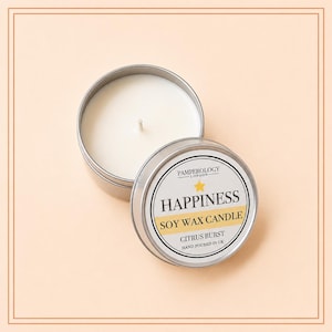 May include: A round silver metal tin containing a white soy wax candle with a single centered wick. The lid is placed beside the tin, featuring a label that reads PAMPEROLOGY LONDON, HAPPINESS, SOY WAX CANDLE, CITRUS BURST, HAND POURED IN UK.