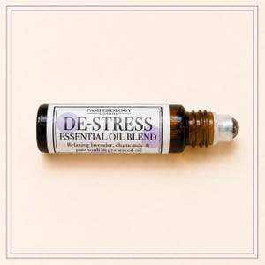 K&ouml;nnte beinhalten: Eine kleine Roll-on-Flasche aus bernsteinfarbenem Glas mit einer &auml;therischen &Ouml;lmischung. Das wei&szlig;e Etikett tr&auml;gt den Text PAMPEROLOGY LONDON, DE-STRESS ESSENTIAL OIL BLEND und Relaxing lavender, chamomile & patchouli in grapeseed oil mit violetten Kreisen.