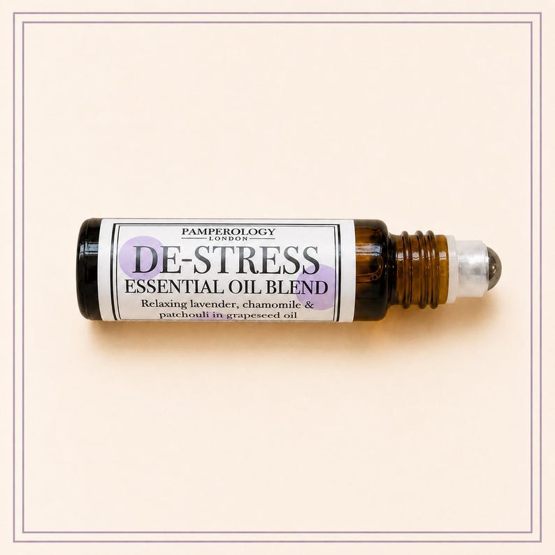K&ouml;nnte beinhalten: Eine kleine Roll-on-Flasche aus bernsteinfarbenem Glas mit einer &auml;therischen &Ouml;lmischung. Das wei&szlig;e Etikett tr&auml;gt den Text PAMPEROLOGY LONDON, DE-STRESS ESSENTIAL OIL BLEND und Relaxing lavender, chamomile & patchouli in grapeseed oil mit violetten Kreisen.
