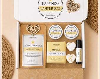Könnte beinhalten: Eine weiße Geschenkbox mit der Aufschrift Happiness Pamper Box enthält ein Grapefruit-Geranien-Bad, eine Sojawachskerze mit Limette und Mandarine, eine rosa Tonerde-Gesichtsmaske, eine Orangen-Seife, zwei herzförmige Objekte und ein kleines Fläschchen.