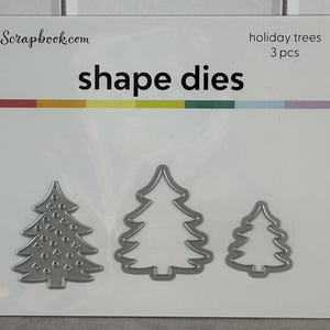 May include: A package of shape dies from Scrapbook.com, featuring three Christmas tree designs. The package includes the text "shape dies" and "holiday trees 3 pcs". The dies are made of silver metal.