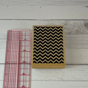 Könnte beinhalten: Ein klarer, roter Kunststoff-Lineal mit Zoll- und Zentimetermarkierungen neben einem Holzblock mit einem schwarzen und beigefarbenen Zickzackmuster. Das Lineal ist etwa 20 cm lang.