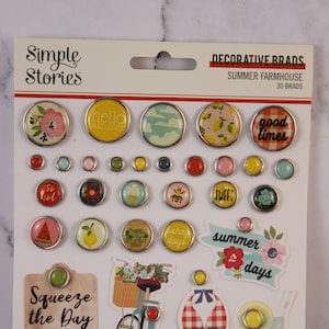 Könnte beinhalten: Eine Packung dekorativer Brads mit Sommer-Bauernhaus-Thema. Die Brads weisen verschiedene Designs auf, darunter Blumenmuster, Zitronen und die Texte "hello summer" und "good times". Es gibt auch Aufkleber mit einem Fahrrad, einem Badeanzug und Limonade.