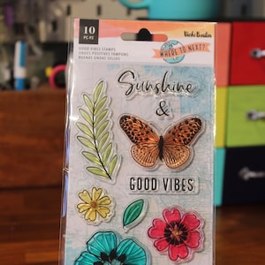 May include: A clear plastic sheet with 10 clear rubber stamps featuring a butterfly, flowers, leaves, and the text "Sunshine & Good Vibes". The sheet is packaged in a clear plastic sleeve with the text "Where to Next?" and "Good Vibes Stamps" on it.