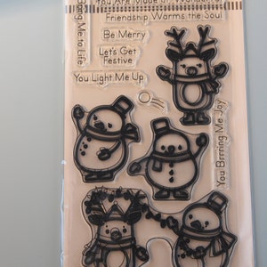 May include: Clear stamp set featuring outlined illustrations of snowmen and a reindeer, with phrases like "Grateful for a Friend Like You" and "Let's Get Festive." Made in the USA.