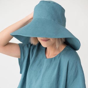 May include: A teal sun hat with a wide brim, and a matching teal top. The hat is made of a soft fabric and offers good shade. The top has a simple, relaxed design. The overall look is casual and summery, perfect for warm weather.