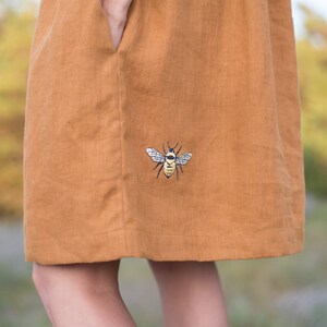 May include: A brown linen dress with an embroidered bee design on the front.