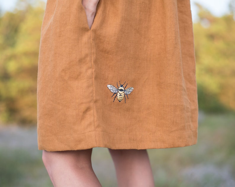 May include: A brown linen dress with an embroidered bee design on the front.