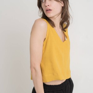 May include: A woman wearing a mustard yellow sleeveless top with a v-neckline and black pants.