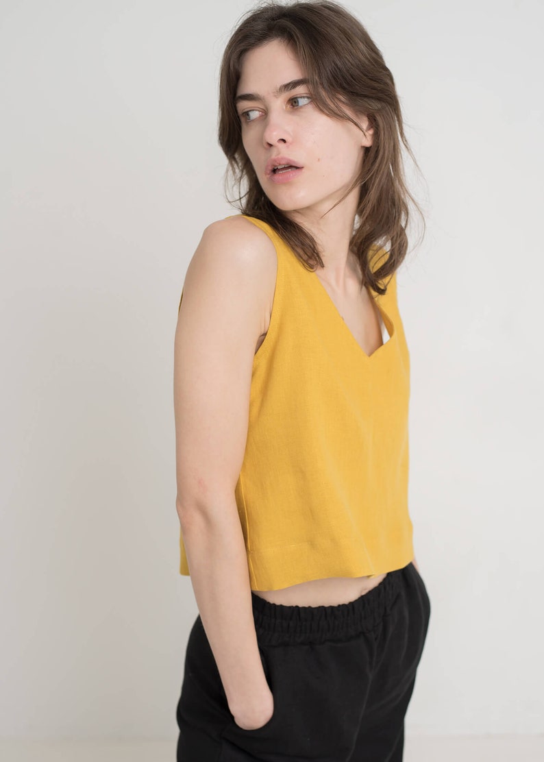 May include: A woman wearing a mustard yellow sleeveless top with a v-neckline and black pants.