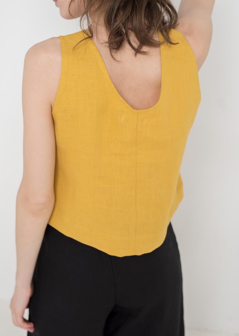 May include: A mustard yellow sleeveless linen top with a scoop neck. The top is cropped and has a slightly curved hemline.