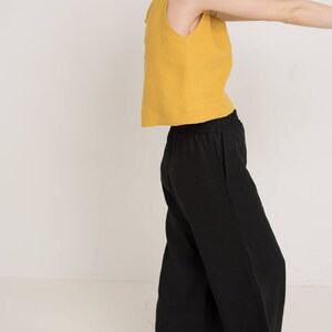 May include: A woman wearing a mustard yellow sleeveless top and black wide-leg pants.
