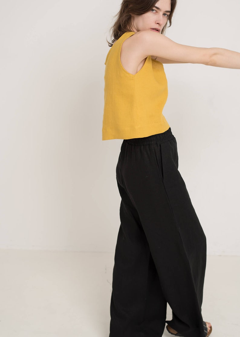 May include: A woman wearing a mustard yellow sleeveless top and black wide-leg pants.