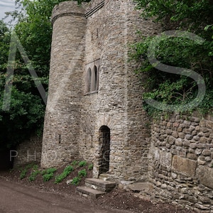 Puede incluir: Una torre de piedra con una puerta y una ventana, rodeada de árboles y follaje.