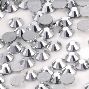 May include: A collection of silver rhinestones with a faceted design. The rhinestones have a flat, circular back and a cone-shaped, multi-faceted front. The facets reflect light, creating a sparkling effect. These embellishments are ideal for various craft projects.