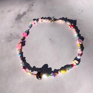 May include: A colourful beaded necklace with various charms, including flowers, butterflies, stars, and a mushroom. The necklace is made of white, pink, purple, blue, green, yellow, and red beads.