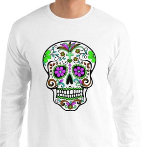 May include: White long-sleeve t-shirt with a colorful sugar skull design. The skull is decorated with green, purple, and brown floral patterns.