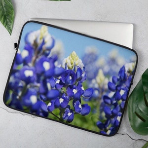 May include: A laptop sleeve featuring a close-up of bluebonnet flowers with white centers against a blue sky background.